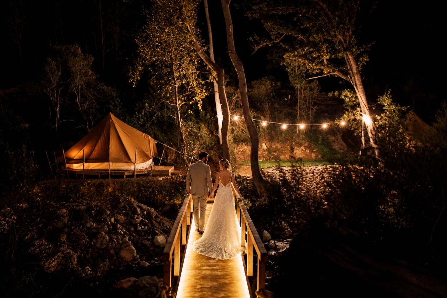 Bride on the wooden bridge beneath festoon lights at night